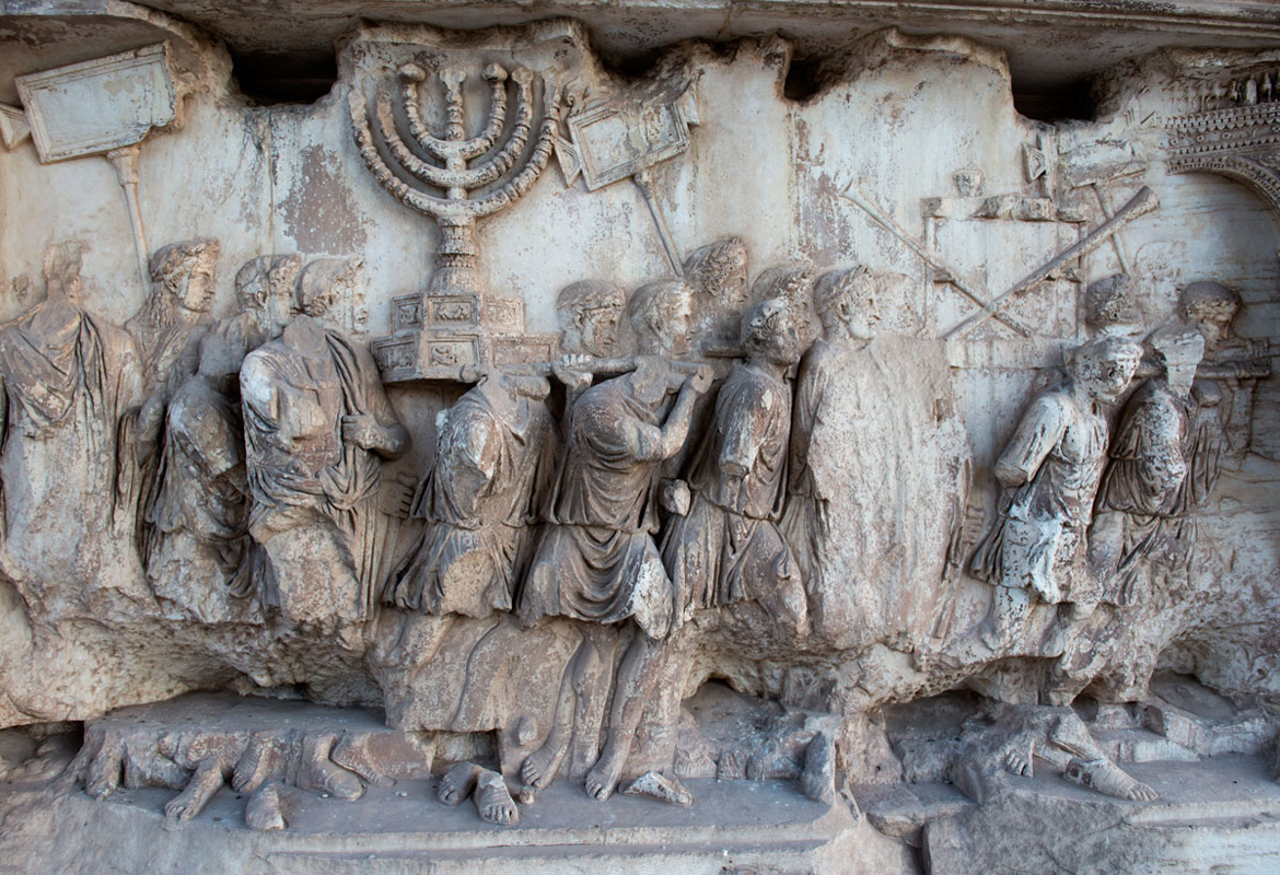 上图:提多凯旋门(Arch of Titus)上的浮雕,上面清楚描绘了第二圣殿时的金灯台和陈设饼桌子,桌上放着几个金杯,桌旁又靠着几支祭司的号筒。提多凯旋门是古罗马城遗址的一座大理石单拱凯旋门,用来纪念提多皇帝在主后70年征服和摧毁耶路撒冷。由于提多凯旋门上描绘了破坏耶路撒冷和亵渎圣殿,许多犹太人拒绝从拱门下经过,只有在1948年以色列复国时,大批人群从罗马犹太社区沿着与古罗马凯旋式相反的方向通过提多凯旋门。提多凯旋门拥有现存唯一的对第二圣殿器物的描绘。